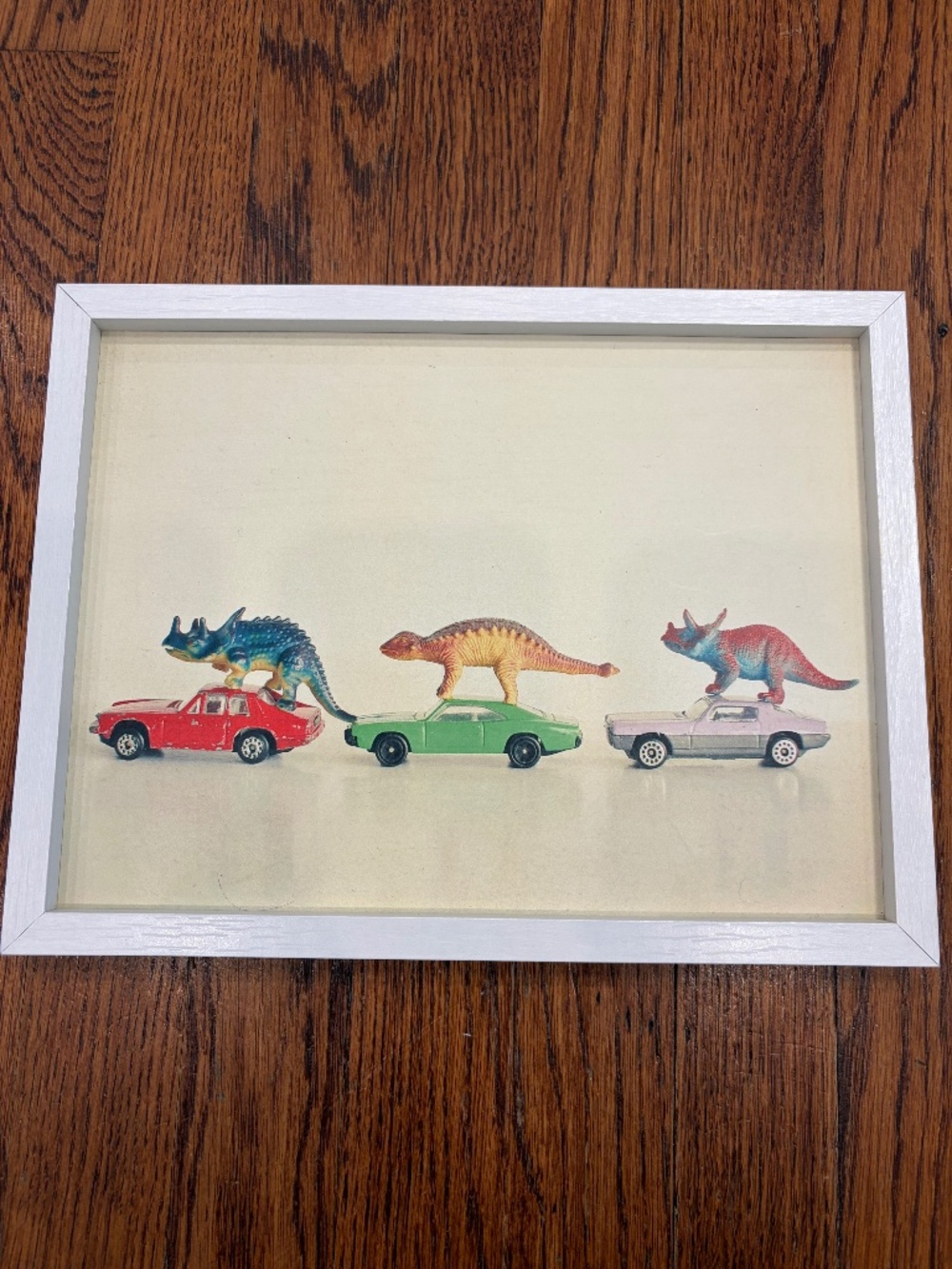 Cassia Beck “Dinosaurs Ride Cars” Framed Art Print – 11x8.5 | White Frame